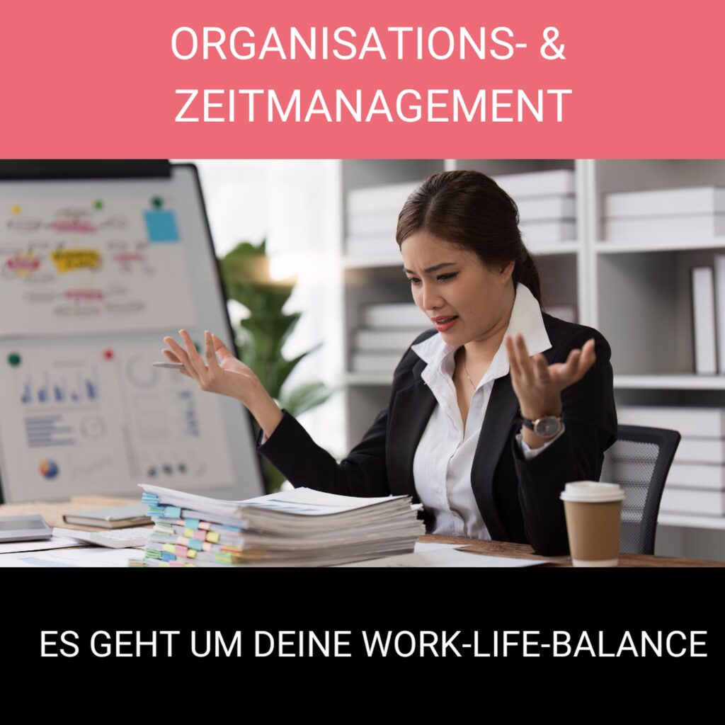 Frau im Business-Outfit sitzt gestresst am Schreibtisch vor einem Stapel Unterlagen, im Hintergrund ein Flipchart: Symbol für Organisations- und Zeitmanagement.