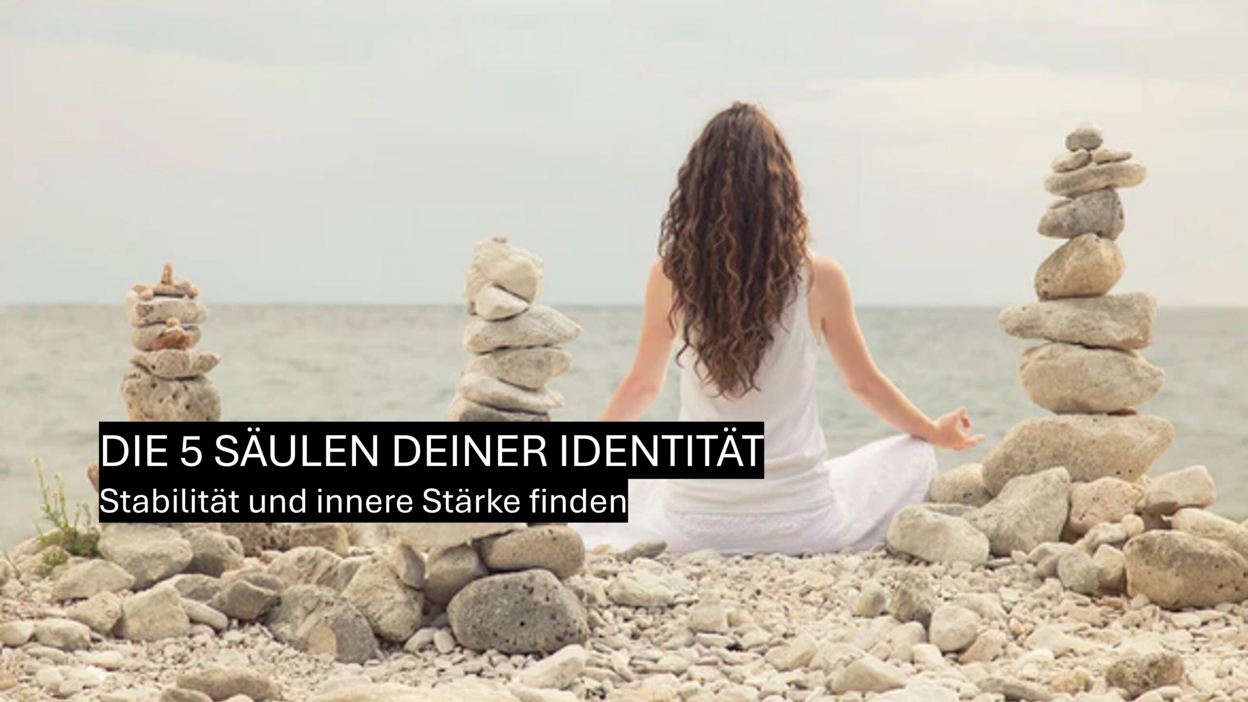Frau sitzt meditierend zwischen aufgeschichteten Steinen am Meer. Symbolbild für die fünf Säulen der Identität, innere Stärke und Stabilität.